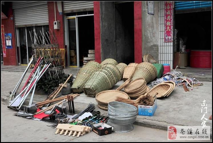 卖日杂用品的老板在三轮车和地上摆放着各种农用具